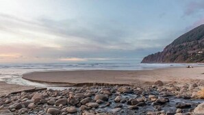 Une plage avec un rivage rocheux au premier plan, une étendue de sable et une falaise en arrière-plan.
