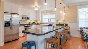 Une cuisine moderne avec des meubles blancs, des appareils en acier inoxydable et un îlot central doté de tabourets de bar.