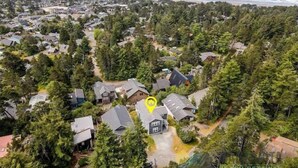 Une vue aérienne d’un quartier résidentiel, avec des maisons entourées d’une végétation luxuriante, une vue dégagée sur l’océan et un marqueur jaune indiquant un emplacement précis.
