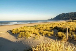 A beach with sand and grassy dunes, a wooden post, and a mountain in the background.