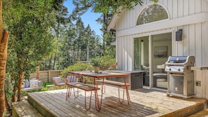 A deck with outdoor furniture, a grill, and a view of a forested area.