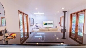 A modern kitchen with a central island, a dining area with a sofa, and a large TV screen displaying a logo.
