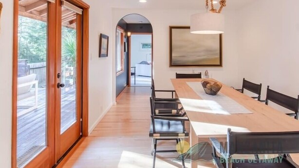 A dining area with a long wooden table, black chairs, and a hanging light fixture.