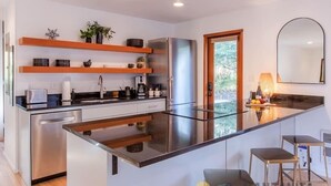 A modern kitchen with a central island, stainless steel appliances, wooden shelves, and a large window.