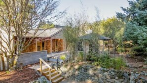 A rustic cabin with a stone exterior, wooden deck, and a stone pathway leading to the entrance.