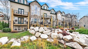 A row of multi-story residential buildings with balconies, stone accents, and a landscaped front yard with rocks and shrubs. - MH603 | Pinecone Retreat: Adventure Awaits in Eden, UT! (Eden)