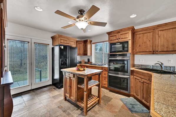 A kitchen with wooden cabinets, a central island, a ceiling fan, and a large window. - MH603 | Pinecone Retreat: Adventure Awaits in Eden, UT! (Eden)