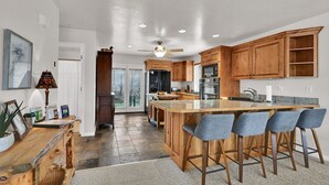 A modern kitchen with wooden cabinets, a central island with bar stools, and a ceiling fan. - MH603 | Pinecone Retreat: Adventure Awaits in Eden, UT! (Eden)
