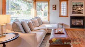 A cozy living room with a sofa, a coffee table, and a fireplace. There are large windows offering a view of the outdoors. - Sea Star by Manzanita Beach Getaway: 3BR Family & Dog-Friendly Near Beach (Manzanita)