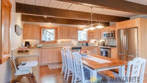 A modern kitchen with wooden cabinets, stainless steel appliances, and a dining area with white chairs. - Sea Star by Manzanita Beach Getaway: 3BR Family & Dog-Friendly Near Beach (Manzanita)