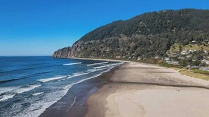 Paisaje costero con una playa arenosa, olas del océano y una ladera boscosa.