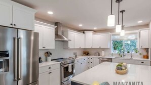Una cocina moderna con armarios blancos, electrodomésticos de acero inoxidable e iluminación colgante.