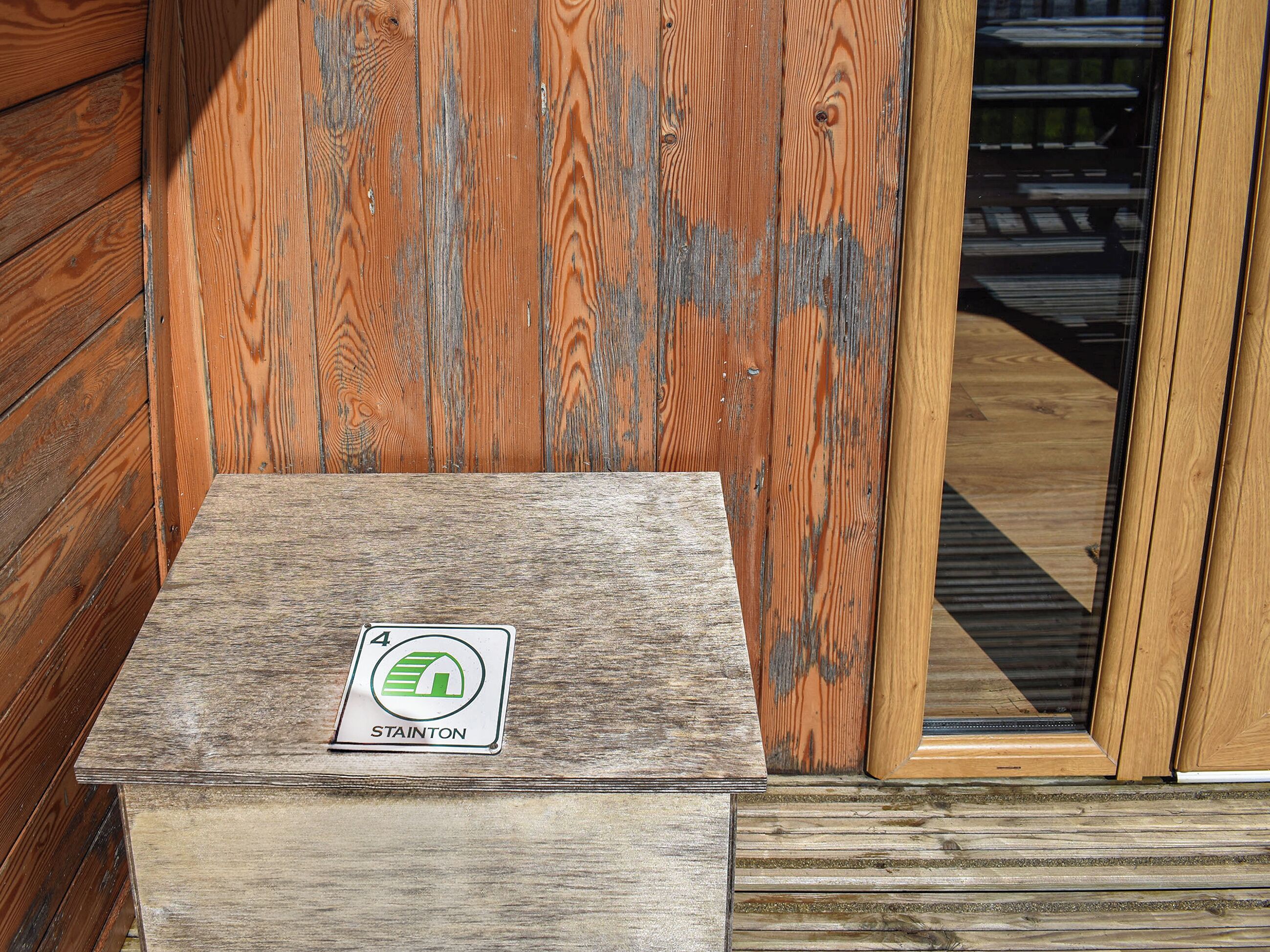 A wooden cabin with a wooden door and a small wooden box with a sign on it.
