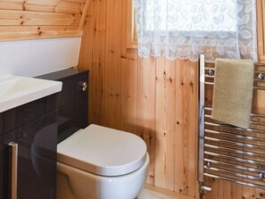 A wooden-paneled bathroom with a white toilet, a sink, and a towel rack with a towel.