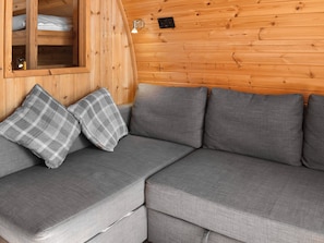 A modern log cabin interior with a gray sectional sofa, plaid throw pillows, and a wooden wall with a small window.