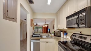 A kitchen with white cabinets, a stainless steel dishwasher, a black stove, and a microwave.