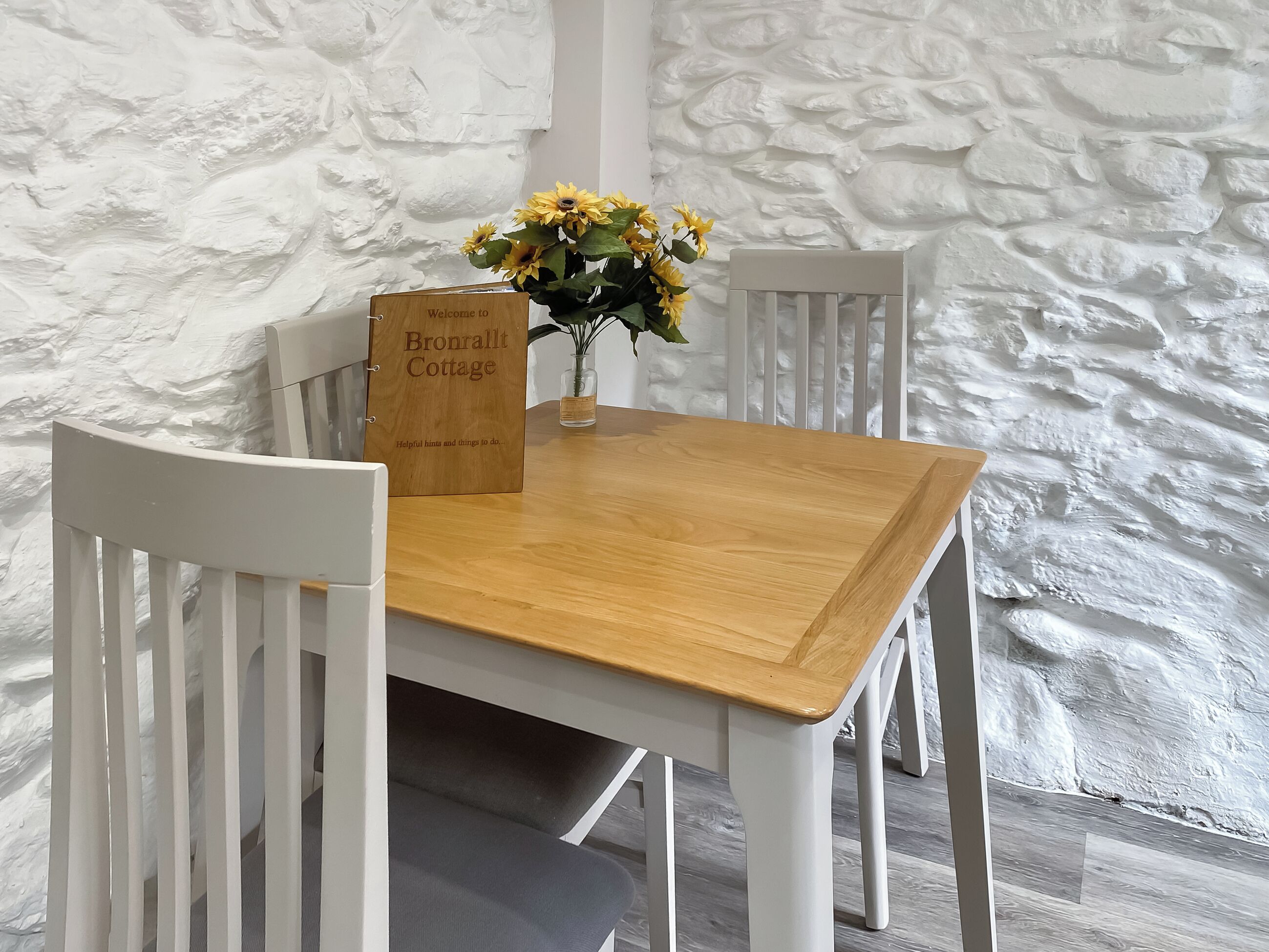 A wooden table with a sign reading "Bronrallt Cottage" and a vase with yellow flowers.
