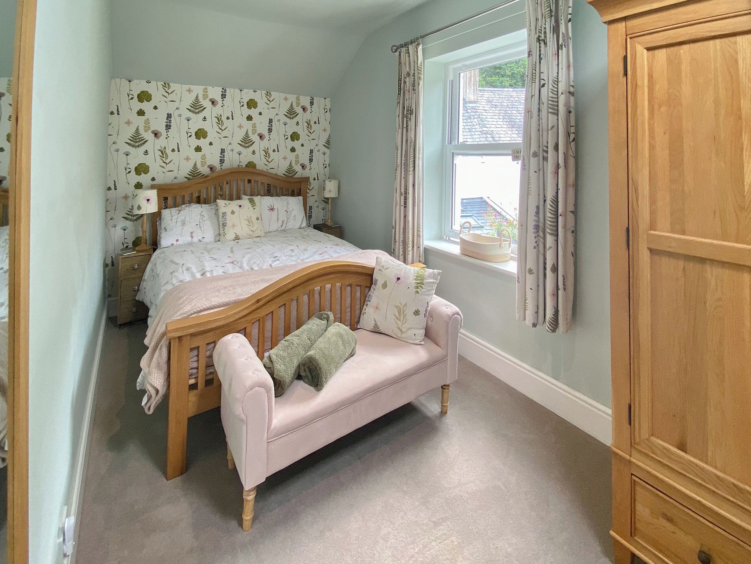 A bedroom with a wooden bed, a pink sofa, a window with curtains, and a wooden wardrobe.