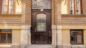 A brown double door with a number '13' above it, flanked by brick buildings with windows.