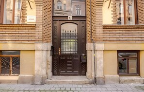 Une porte double marron, surmontée du chiffre « 13 », est encadrée par deux bâtiments en briques dotés de fenêtres.