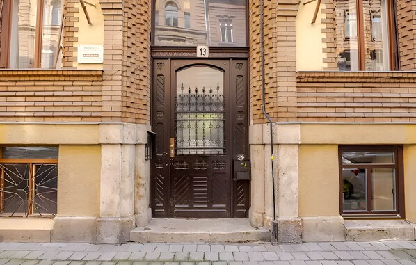 Una puerta doble marrón con el número '13' encima, flanqueada por edificios de ladrillo con ventanas.