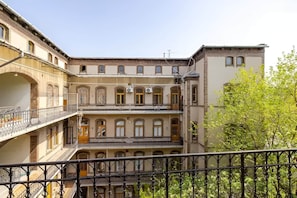 Un edificio de varios pisos con balcones, una escalera y un árbol en primer plano.