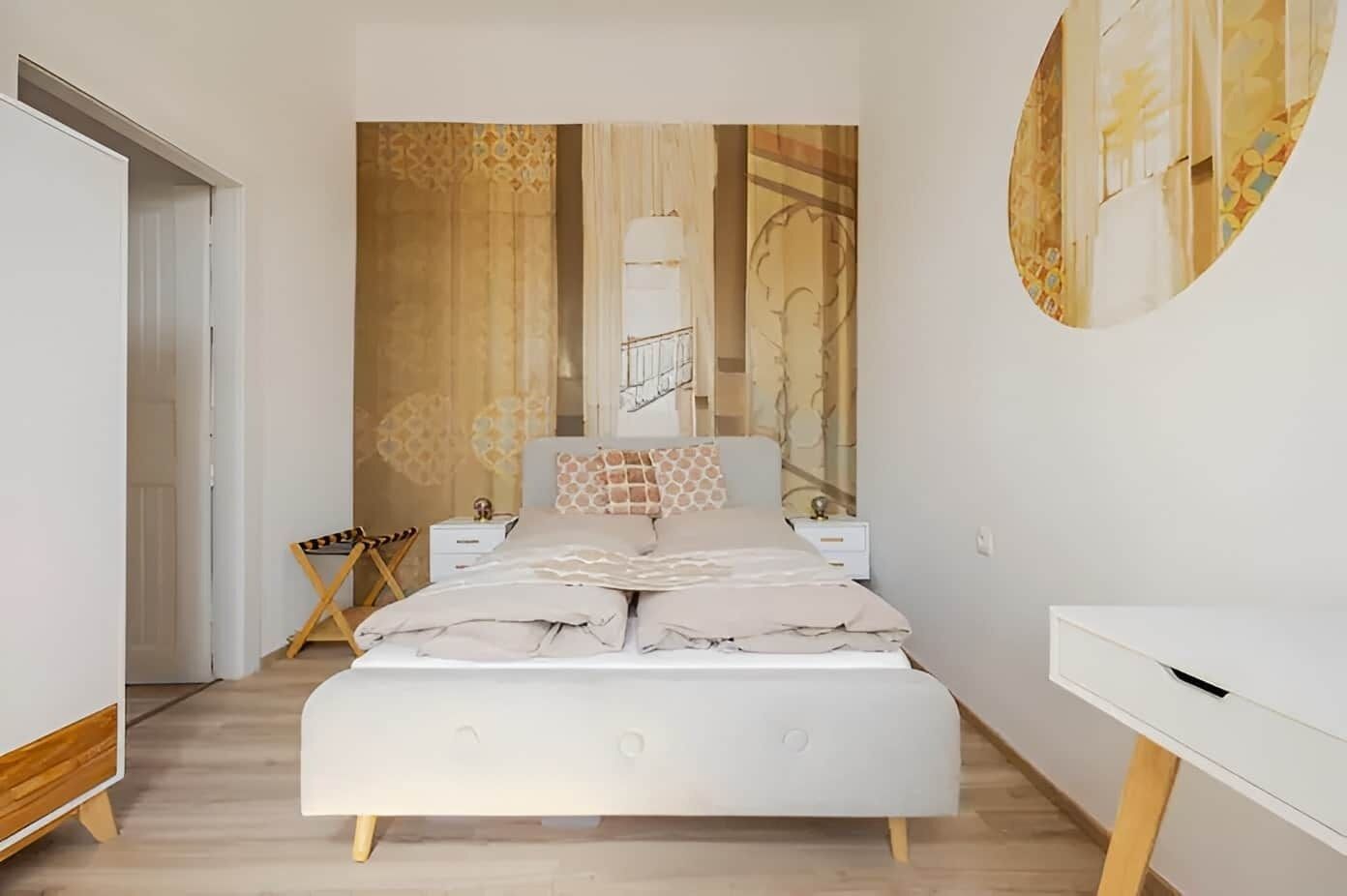 A modern bedroom with a white bed, a desk, and a large tapestry on the wall.