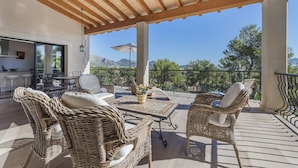 An outdoor patio with wicker furniture, a table, and a view of mountains. - Villa Can Oronella by Balearic Villas (Pollensa)