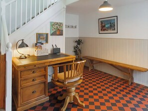 Une pièce comprenant un bureau, une chaise et un banc. On y trouve un escalier avec des rampes blanches et un luminaire suspendu.