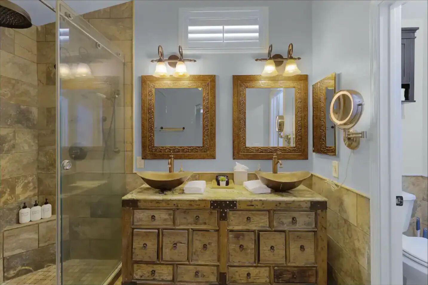 A bathroom with a glass shower enclosure, two large mirrors with ornate frames, and a wooden vanity with multiple drawers.