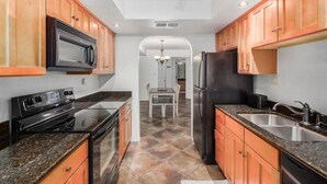 Una cucina con pensili e basi in legno, un forno a microonde, un fornello e un frigorifero.
