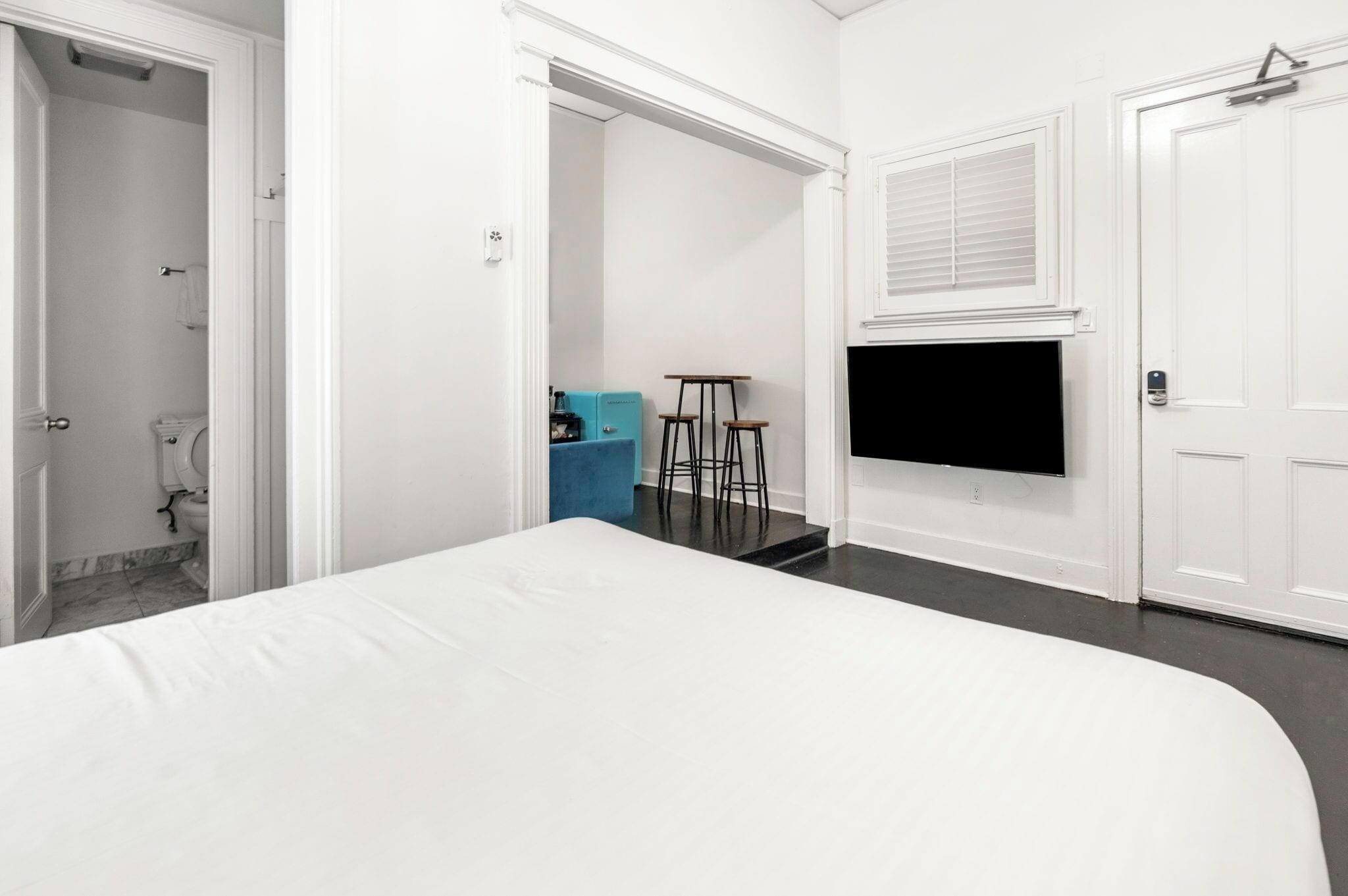A bedroom with a bed, a TV mounted on the wall, and a bathroom visible through an open door.