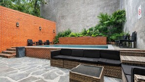 A poolside area with a brick wall, outdoor seating, and a stone floor. - Roami at St. Helene (New Orleans)