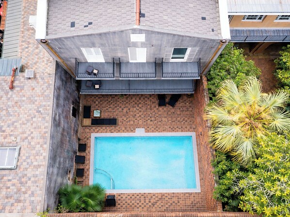 A rooftop pool with a brick wall, a small deck, and surrounding greenery.
