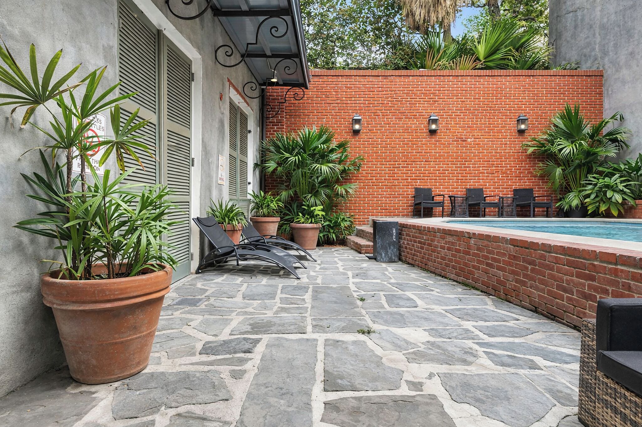 A patio area with a brick wall, potted plants, outdoor seating, and a swimming pool.