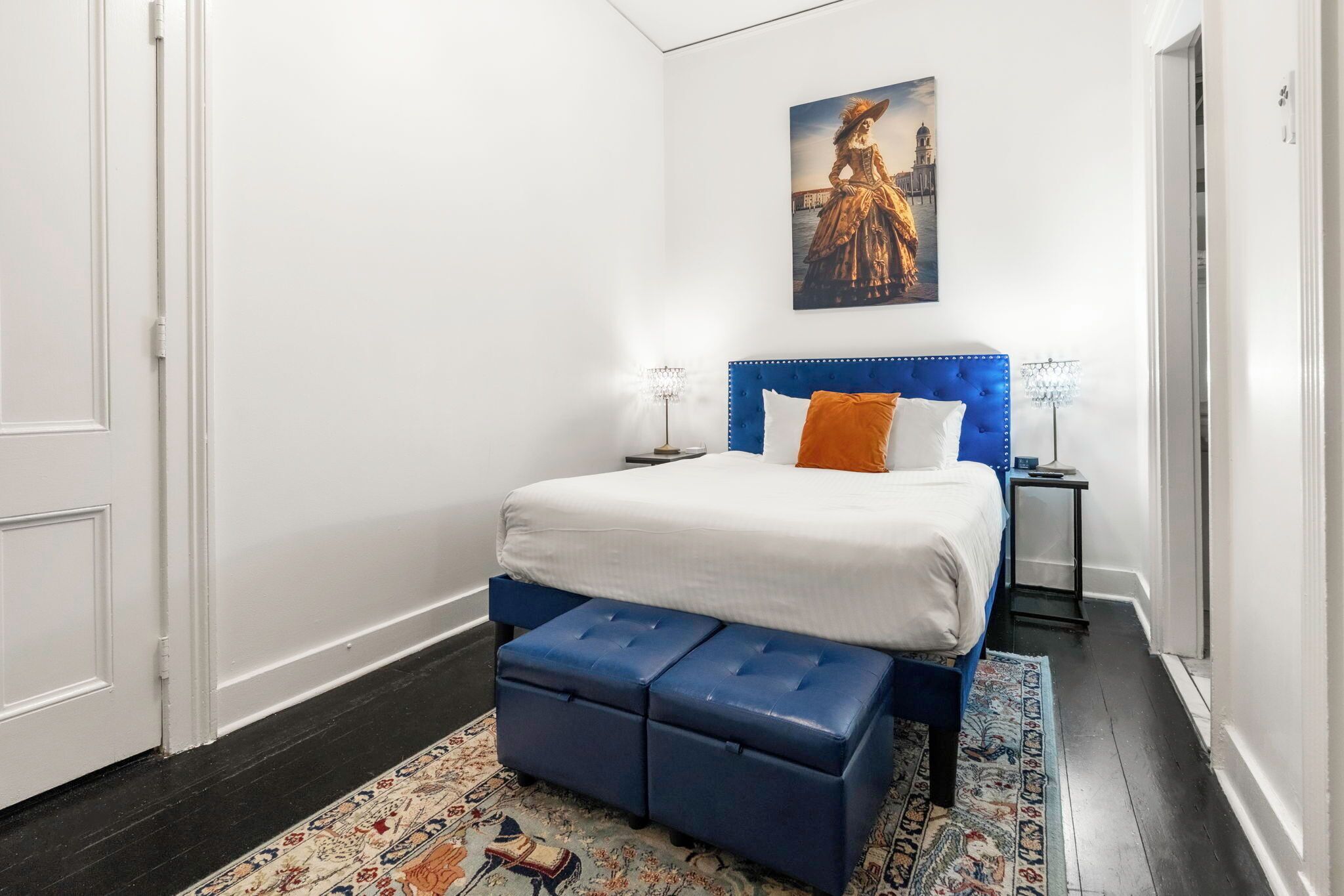 Ein Schlafzimmer mit einem Bett, einer blauen Polsterbank, einem gemusterten Teppich und einem Bild an der Wand.