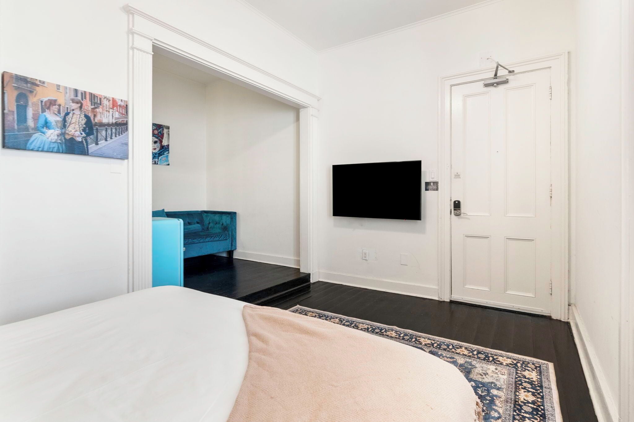A bedroom with a bed, a TV mounted on the wall, a door, and a blue chair.
