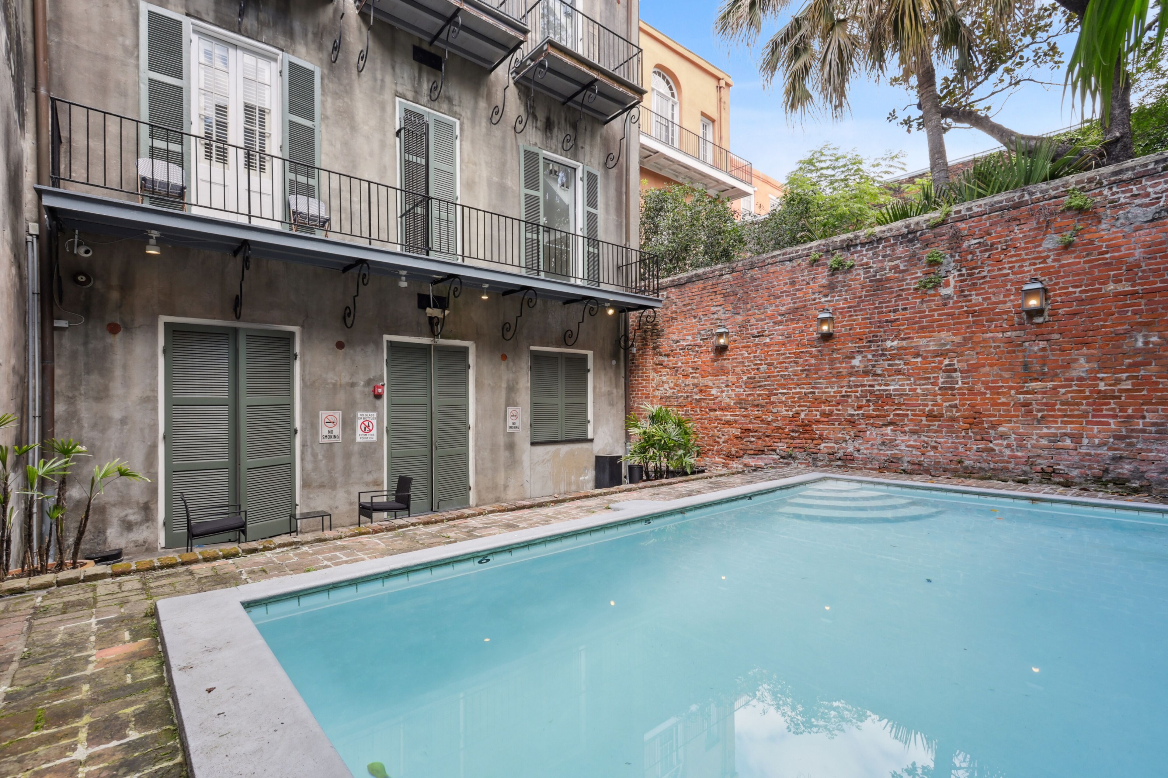 A swimming pool adjacent to a building with a brick wall and a balcony.