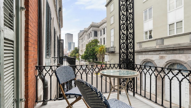 A balcony with a table and two chairs, a brick wall, and a wrought iron fence. - Roami at St. Helene (New Orleans)