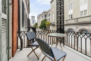 A balcony with a table and two chairs, a brick wall, and a wrought iron fence.