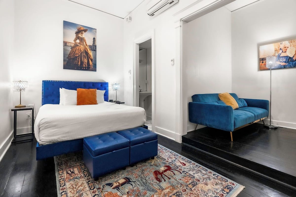 A bedroom with a bed, a blue sofa, a patterned rug, and two wall-mounted artworks.
