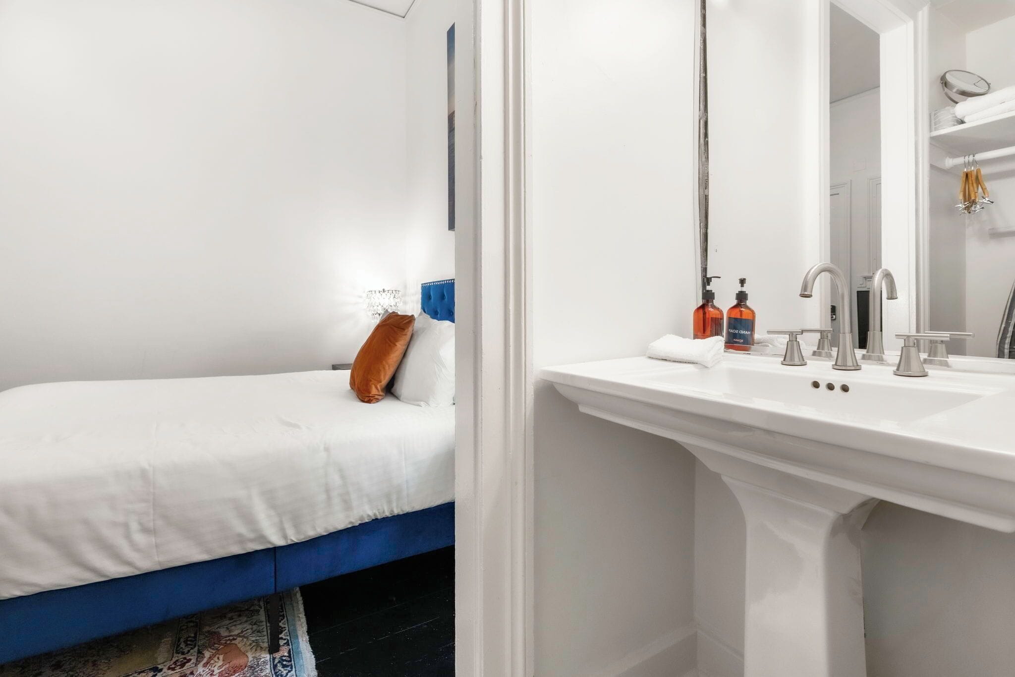 Un lit blanc avec une tête de lit bleue, un lavabo blanc avec un miroir et une serviette posée sur le comptoir.