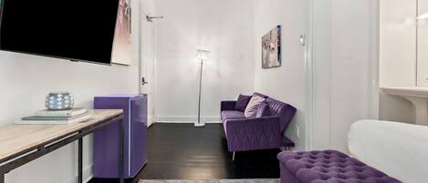 A modern living room with a purple sofa, a white couch, a flat-screen TV, and a floor lamp.