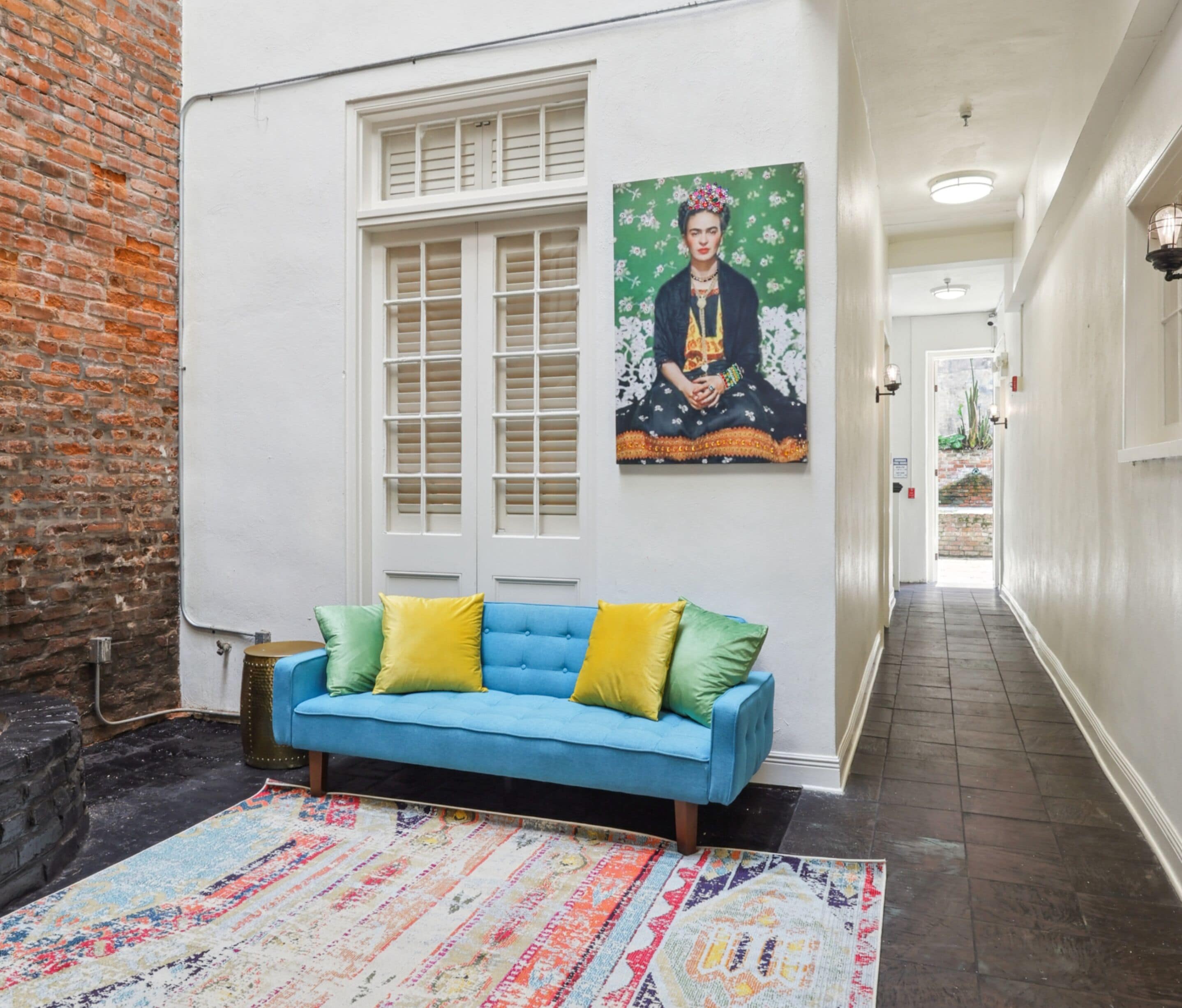 Un couloir avec un canapé bleu, un tapis à motifs, un mur en briques, une porte blanche et un tableau accroché au mur.