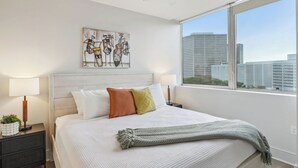 Ein modernes Hotelzimmer mit einem großen Bett, Blick auf die Stadt und einem Deckenventilator.