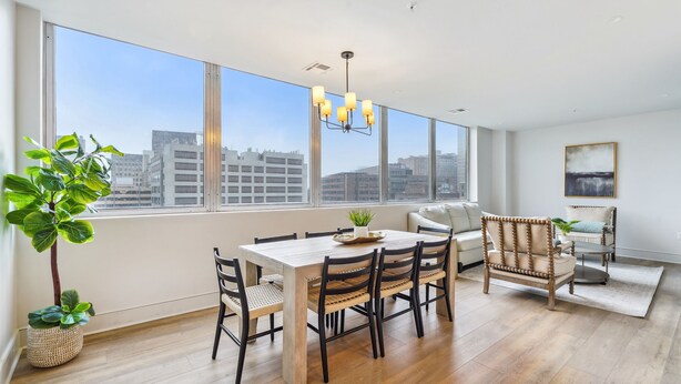 A spacious room with a large dining table, chairs, a sofa, and a view of the city through large windows. - The Eleanor 4BD/4B - All King Bedrooms, City View (New Orleans)