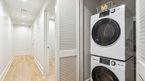 A laundry area with two stacked front-loading washing machines and a hallway with white walls and wooden flooring. - The Eleanor 4BD/4B - All King Bedrooms, City View (New Orleans)