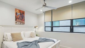 A bedroom with a bed, a ceiling fan, a window with blinds, and a painting on the wall.