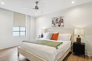 Une chambre moderne avec un grand lit, un ventilateur de plafond, une fenêtre et une œuvre d’art murale.