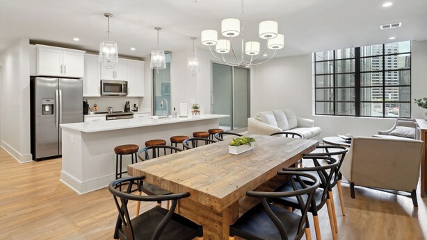 Een moderne keuken met een centraal eiland, roestvrijstalen apparatuur en een eethoek met een houten tafel en stoelen.